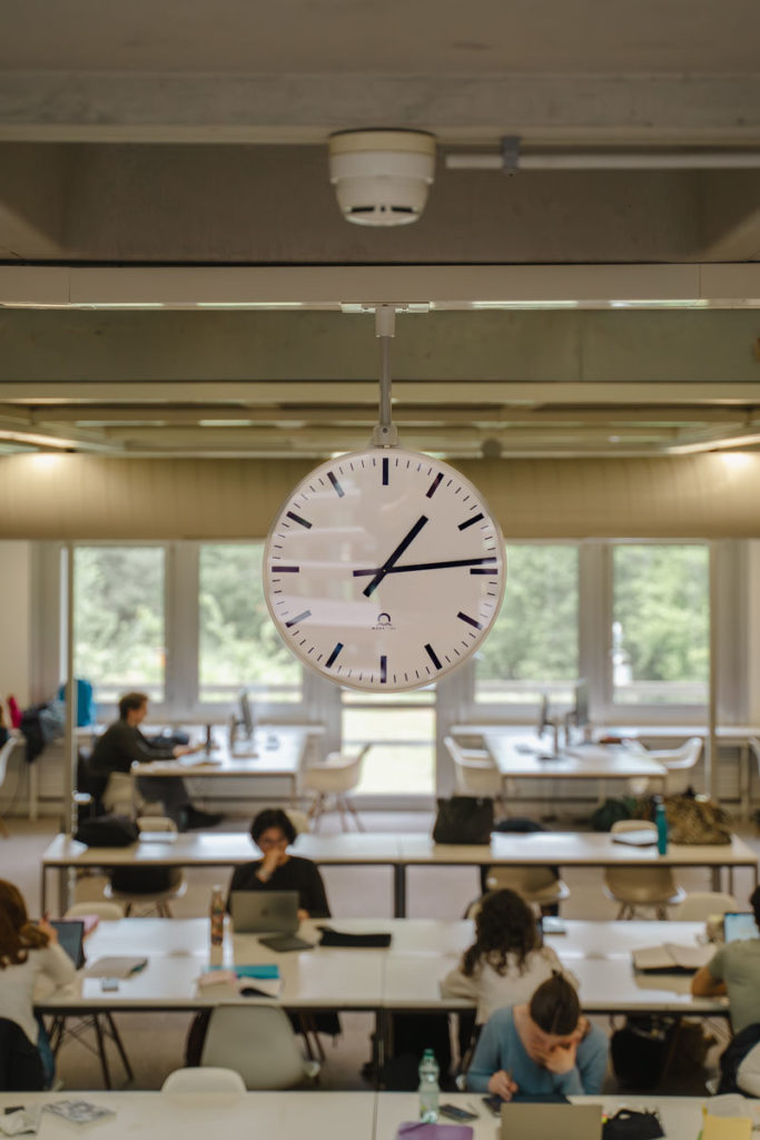 Photographie de la salle d’étude de la bibliothèque, avec lecteurs et grande horloge centrale